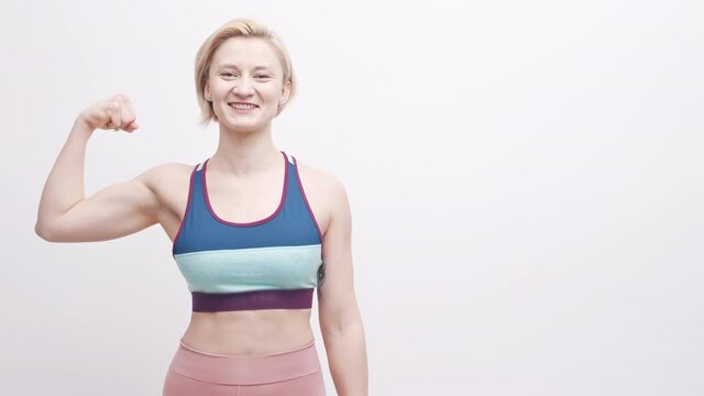 Young blond woman in activewear flexing her muscle