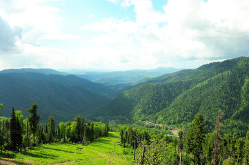 The view from the top of the mountain to the high hills overgrown with forest and the cable car of the chair lift descending into the valley.