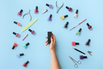 Female hand with nail buffer and tools for manicure on color background