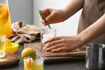 Woman making cocktail with rosemary on table in kitchen