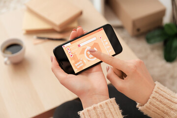 Woman using mobile phone with open page of delivery service application at home, closeup