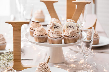 Dessert stand with tasty wedding cupcakes and word LOVE on table