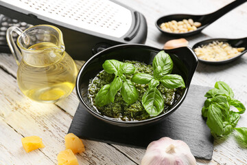 Bowl with tasty pesto sauce on light wooden background, closeup