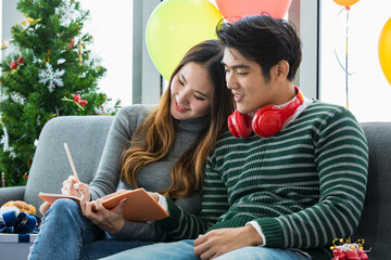 Young Asian man with red earphone relax sit together with lovely girlfriend who enjoy jotting...