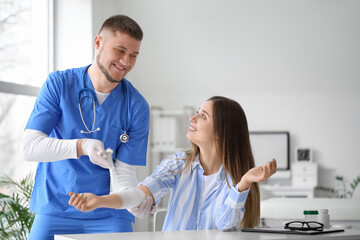 Obraz premium Doctor applying bandage onto arm of young woman in clinic