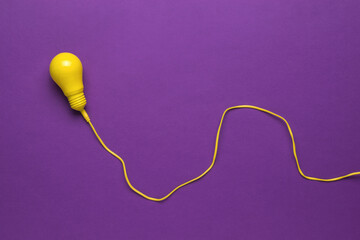 A yellow light bulb on a long yellow wire on a purple background. Minimalism. Flat lay.