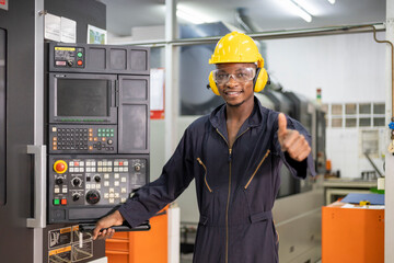 Portrait of African American mechanic engineer worker wearing safety equipment showing thumbs up beside the automatic lathe machine in the manufacturing factory