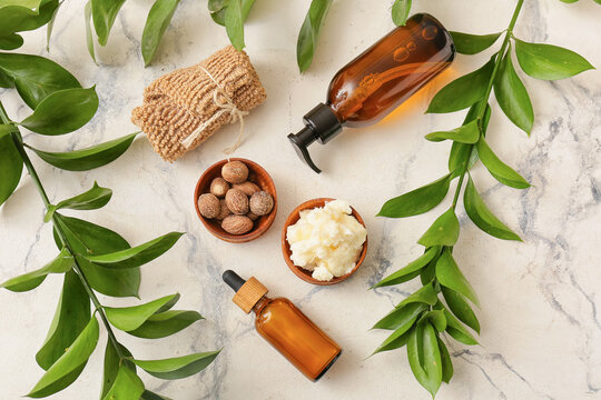Bowl of shea butter, nuts, bath supplies and plant branches on light background