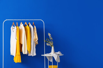 Rack with stylish clothes and table on color background