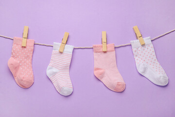 Different baby socks hanging on rope against color background