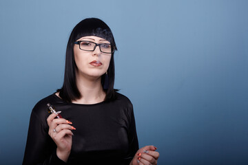 A beautiful girl with dark hair and glasses sensually smokes an electronic cigarette
