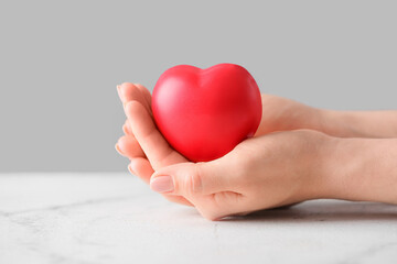 Fototapeta premium Female hands holding red heart on light background, closeup
