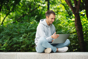 Obraz premium Happy remote worker read email of salary increase or career development on laptop while distant work from outdoors. Positive freelancer guy get job offer from big outsource company. Success concept