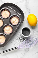 Baking tin with uncooked poppy seed muffins on light background