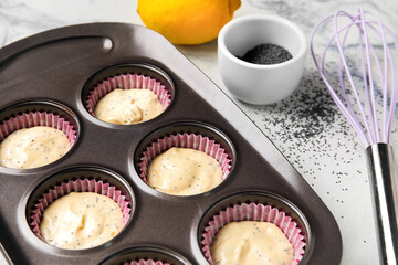 Baking tin with uncooked poppy seed muffins on light background