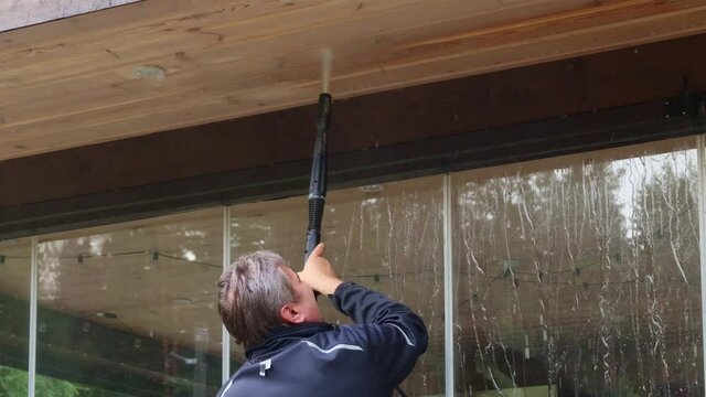 Man cleaning walls and floor with high pressure power washer. Washing terrace wood planks and cladding walls. High quality 4k footage