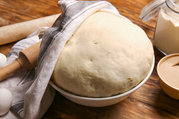Bowl with fresh dough on wooden background