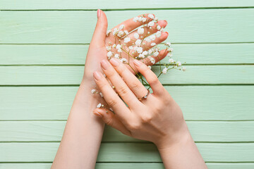 Female hands with engagement ring and gypsophila flowers on color wooden background