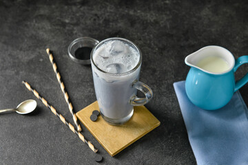 Glass cup of tasty Charcoal Latte and jug with milk on dark background