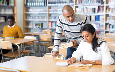Positive young adults communicating while preparing to exam in library