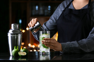 Female bartender making tasty mojito on table in bar
