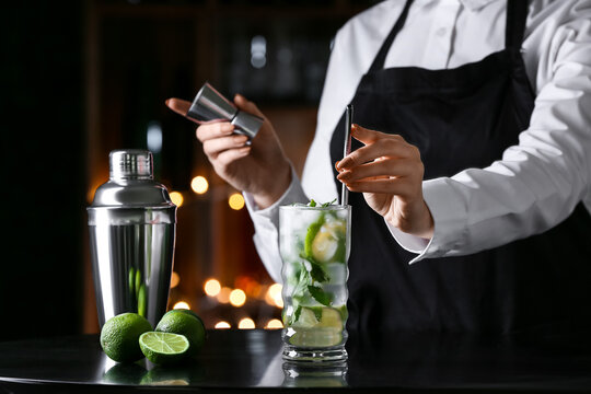 Female bartender making tasty mojito on table in bar