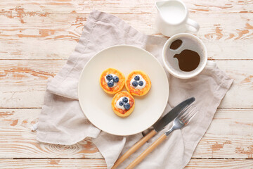 Plate with cottage cheese pancakes, blueberry and cup of tea on light wooden background