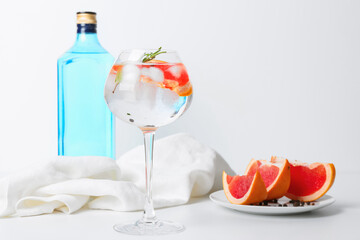 Glass of cold gin tonic and grapefruit slices on light background