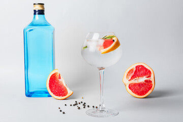 Glass of cold gin tonic and grapefruit slices on light background