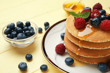 Plate of tasty pancakes with honey and berries on color wooden background, closeup
