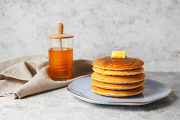 Plate of tasty pancakes with honey and butter on light background