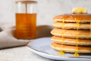 Fototapeta na wymiar Plate of tasty pancakes with honey and butter on light background, closeup