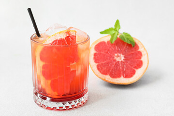 Glass of tasty Tequila Sunrise cocktail and grapefruit on light background