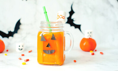 Drink for Halloween. hildren's and party of Halloween treats. Pumpkin orange cocktail in glasses, decorated with creepy faces scary marshmallows on a white marble table. Copy space