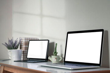 Blank white screen laptop and tablet with magic keyboard on wooden table, home office concept.