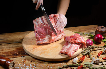The chef uses his hands to slice pork ribs with a knife on a wooden cutting table. Selective focus. The concept of the cooking process.