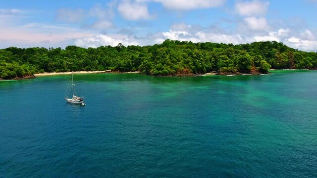 Forward Flight of White Monohull Sailboat near Emerald Water Island Beach Cove 