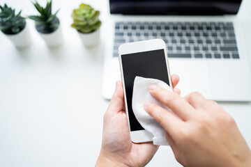 Businessman cleaning a smartphone screen of dust, dirt and fingerprints with a cleaning wipe at his desk.