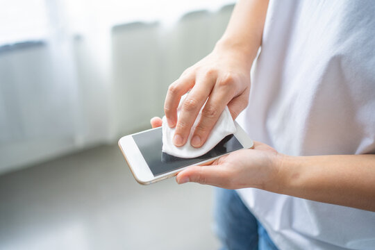 Woman's hand standing wipe smartphone screen with disinfectant cloth at home. Close-up woman cleans her mobile phone. - Powered by Adobe