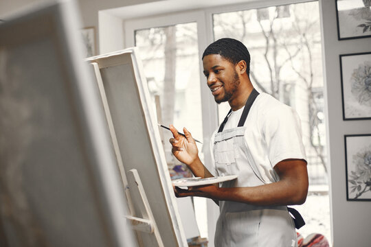 Young African-American artist painting picture in workshop