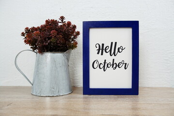 Hello October typography text with artificial plant decoration on wooden table and white wall background