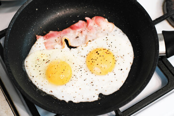 Traditional English breakfast with fried eggs and bacon in cast iron pan on a ccooker. weekend home brakfast time.