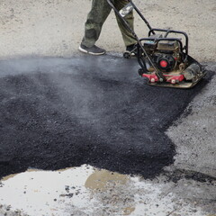 A worker rams new asphalt with a manual motor asphalt rammer, asphalting by the pit method, local road repair