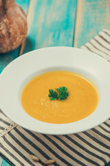 Pumpkin and carrot soup with cream and parsley on blue  wooden background.