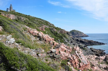 Scenic landscape in the Kullaberg Nature Reserve, Mölle, Skåne, Sweden. Red rocks, summery blue skies and the open Kattegatt sea in the distance. The famous Kullen lighthouse can be seen on the hill.