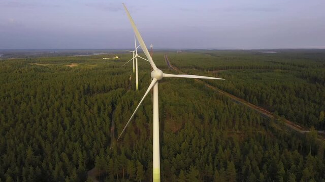 Aerial view away from a wind power turbine, golden hour - pull back, drone shot