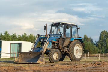 A blue tractor is leveling a construction site for the installation of modular frame houses