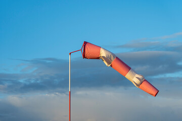 Red and white wind indicator in the shape of a cone at the airfield. Sunset and clouds in the...