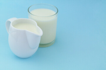 Glass and jug with milk on blue background with copy space