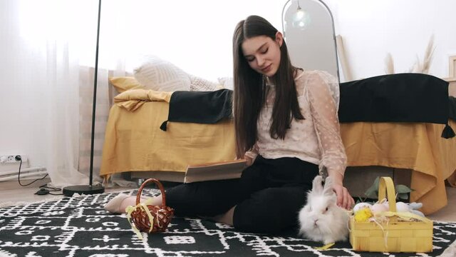 Girl sitting reading a book with rabbit on the floor